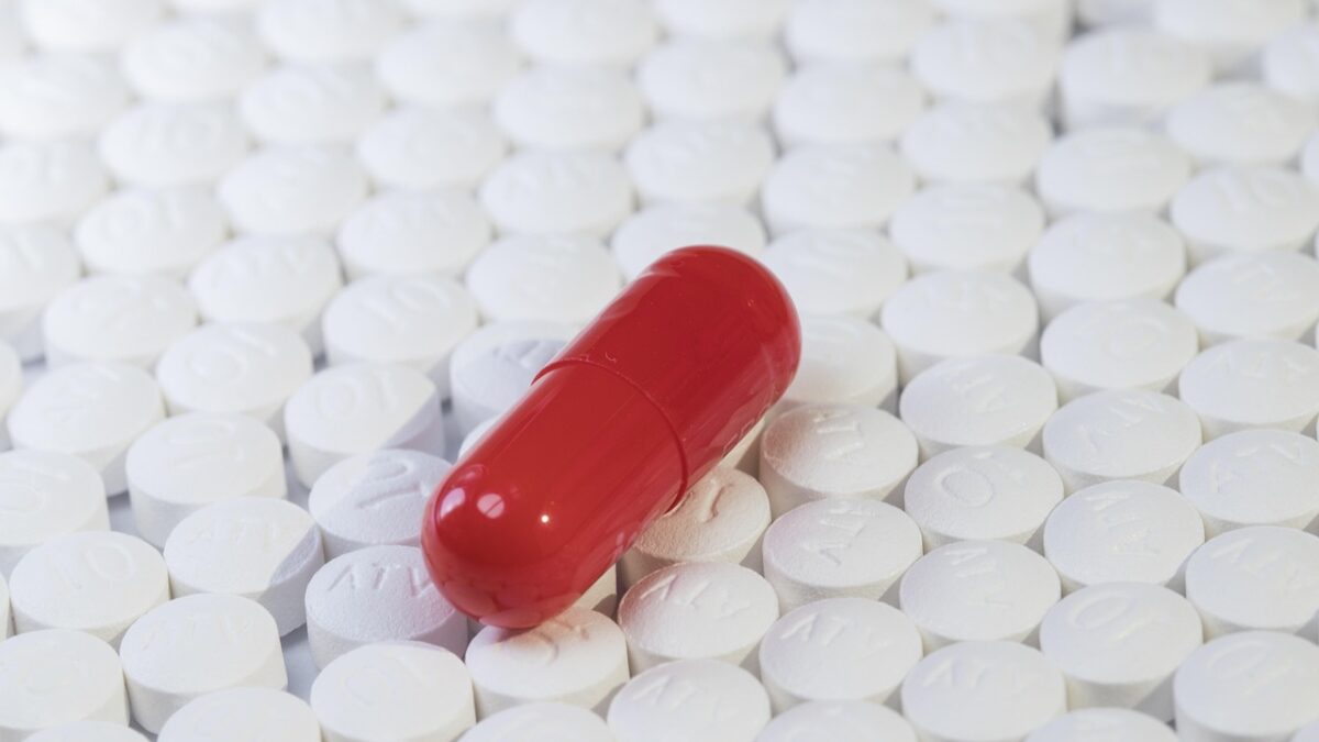 Gros plan de nombreux comprimés blancs gravés de lettres, avec une capsule rouge posée au centre.
