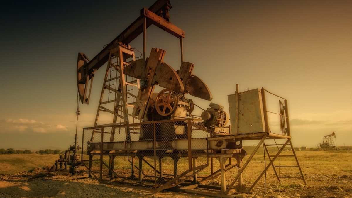 Pompe à balancier de puits de pétrole en métal rouillé dans un champ aride au coucher du soleil, avec un autre puits visible à droite.