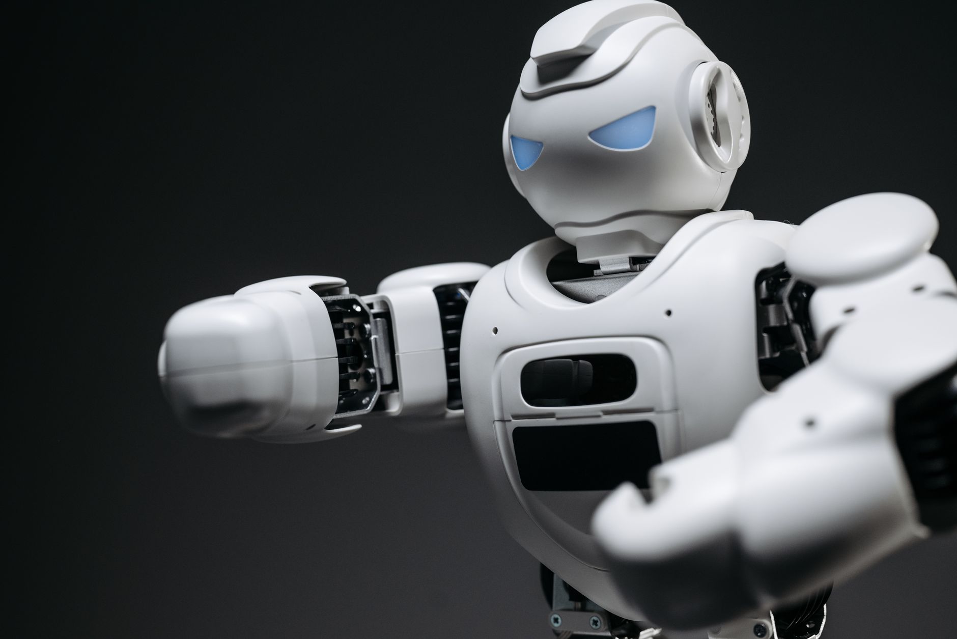 Robot humanoïde blanc aux yeux bleus lumineux, bras tendu vers l'avant, sur un fond gris sombre.