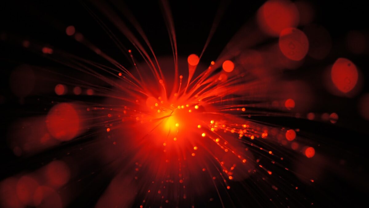 Faisceau de fibres optiques rouge-orangé rayonnant depuis un point central sur fond noir, avec des reflets bokeh.