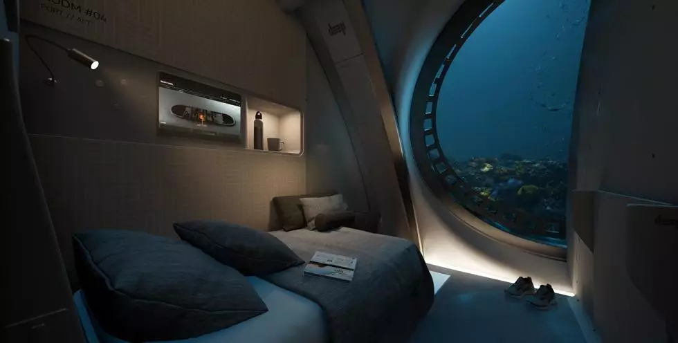 Un lit et un panneau électronique semblable à une télévision à l'intérieur d'un habitat sous-marin. Une fenêtre permet d'observer la vie marine extérieure.