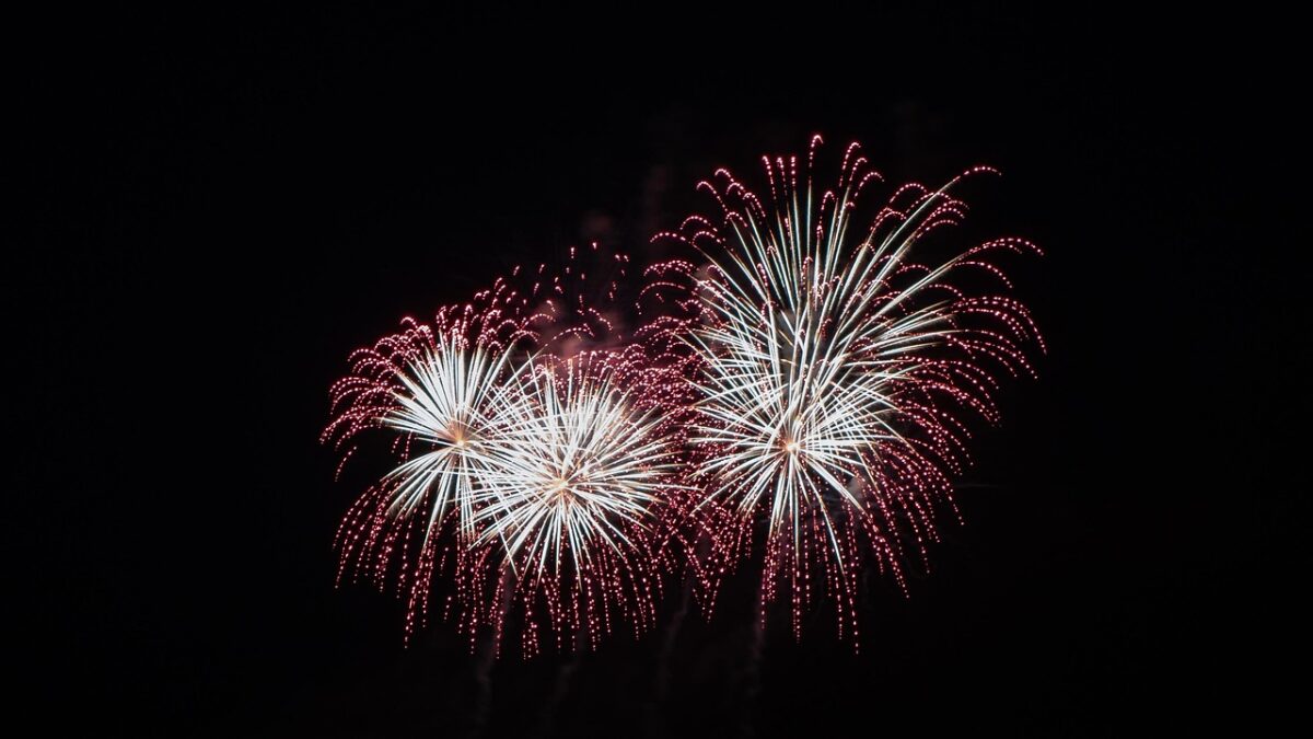 Feux d'artifice en gerbes blanches et rouges dans un ciel nocturne noir.