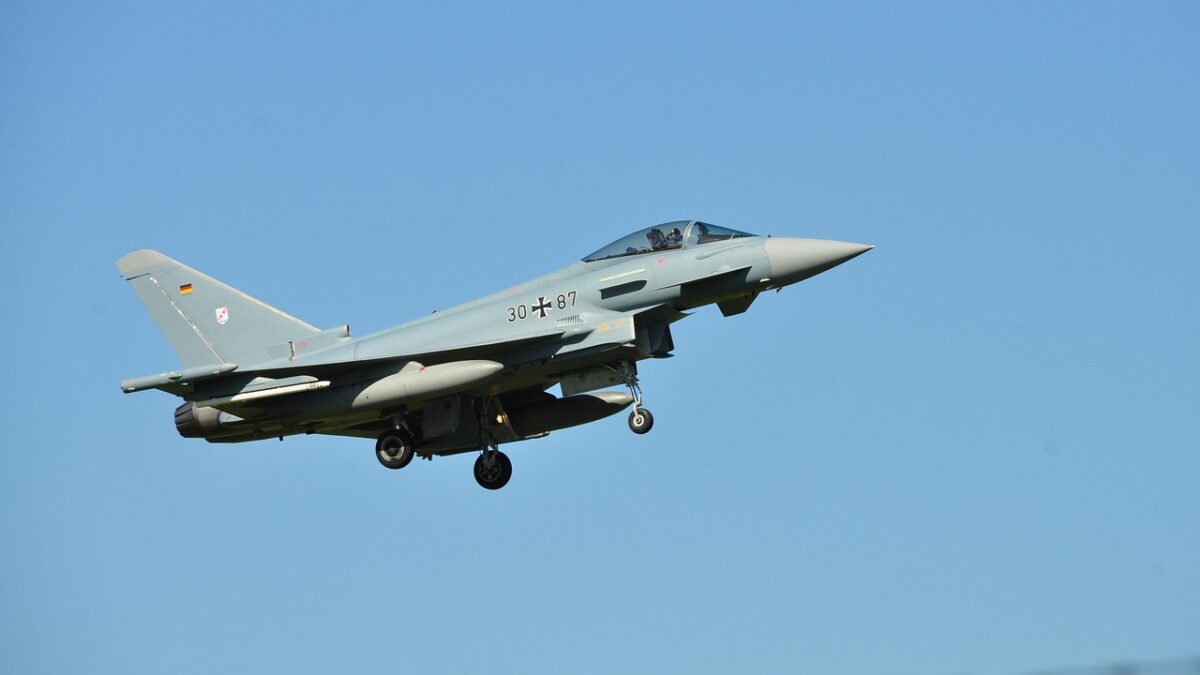 Avion de chasse Eurofighter Typhoon gris en vol contre un ciel bleu, train d'atterrissage sorti, avec croix noire de la Luftwaffe et drapeau allemand sur la dérive.
