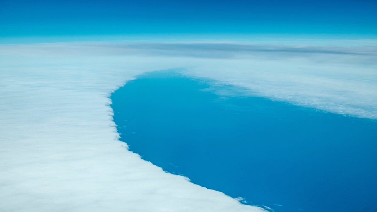 Vue aérienne d'une vaste étendue d'eau bleue, entourée de glace blanche, avec un bord arrondi net sous un ciel bleu dégradé.
