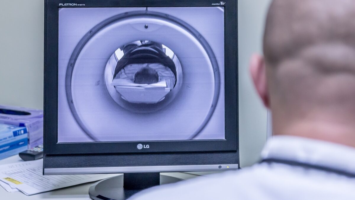 Un médecin en blouse blanche, de dos, observe un moniteur LG affichant l'image d'un appareil d'IRM où un patient est allongé dans le tunnel.