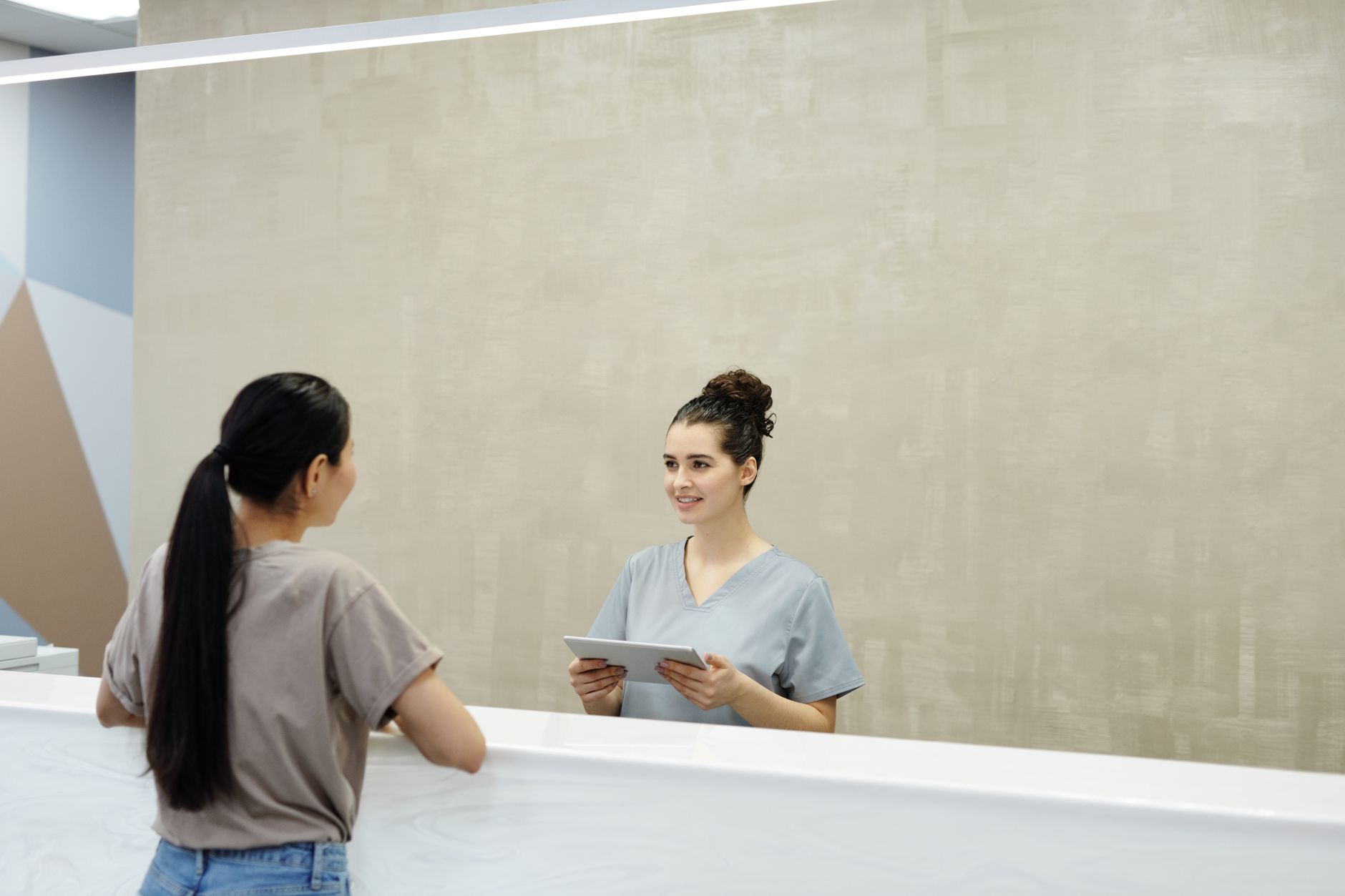 Une réceptionniste souriante avec une tablette aide un patient à la réception d'un établissement médical.