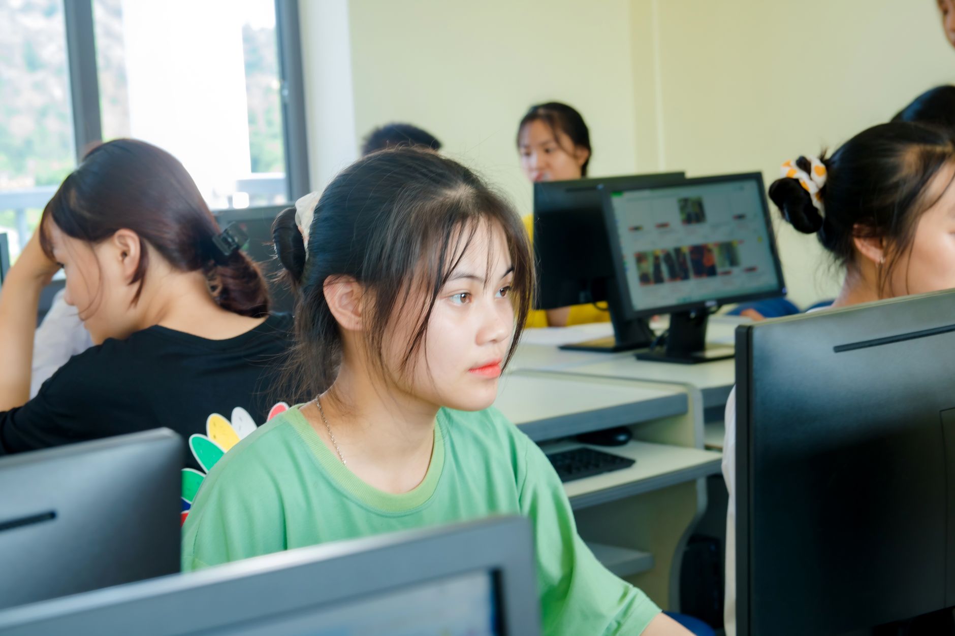 Étudiants asiatiques concentrés sur l'étude de la technologie dans une salle informatique lumineuse.
