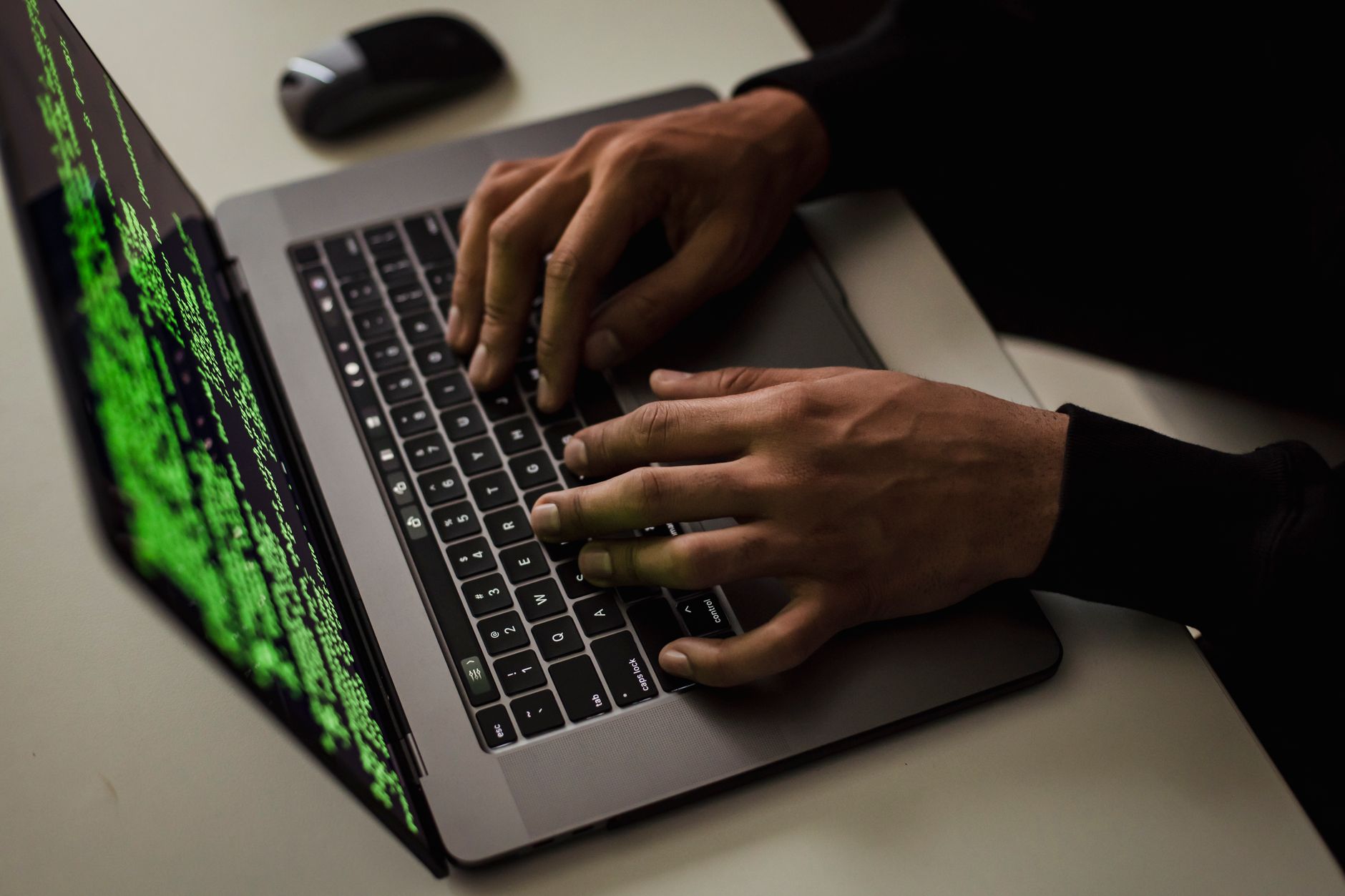 Vue de dessus d'un hacker anonyme tapant sur un netbook avec des données à l'écran tout en étant assis à un bureau