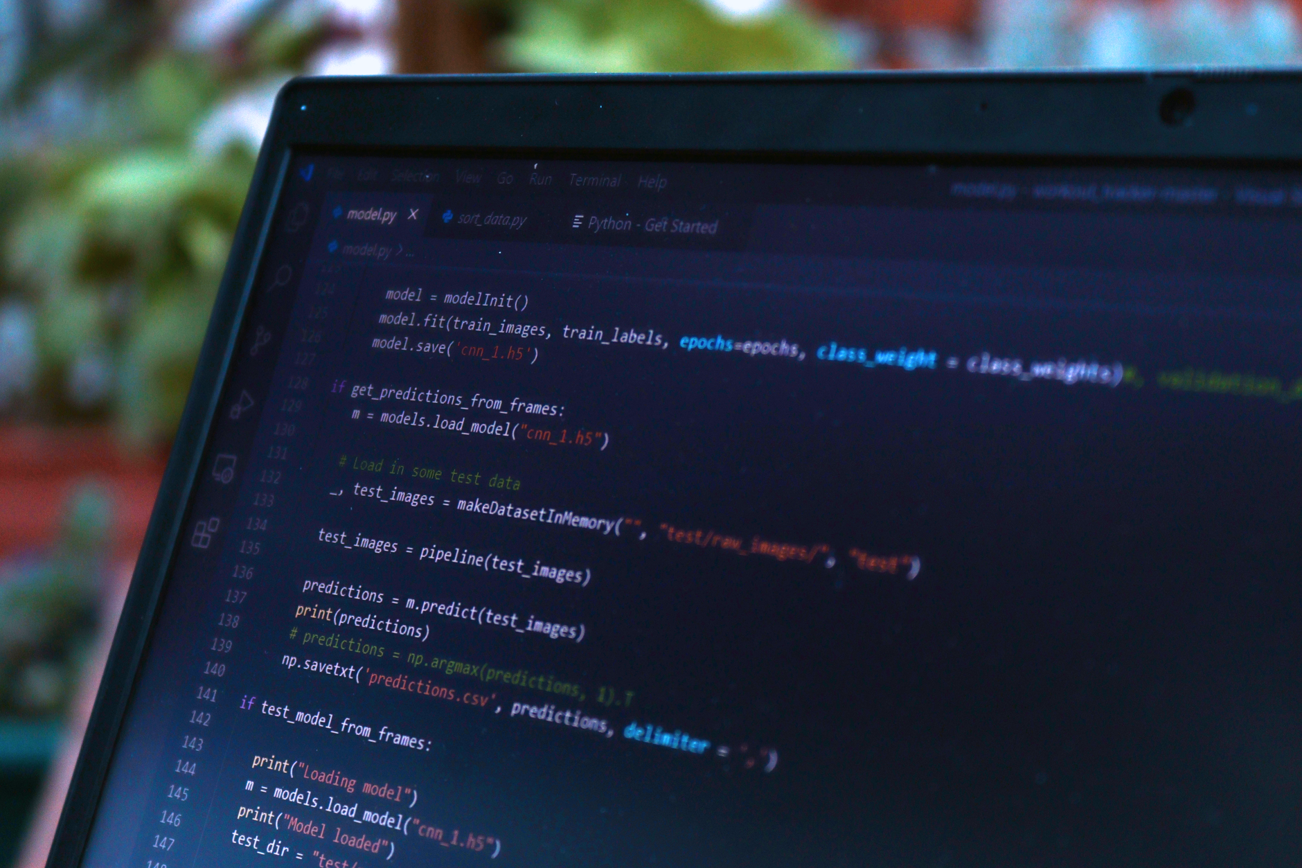 Écran d’ordinateur portable affichant du code Python d’apprentissage automatique dans un éditeur sombre, devant un arrière-plan de feuillage flou.